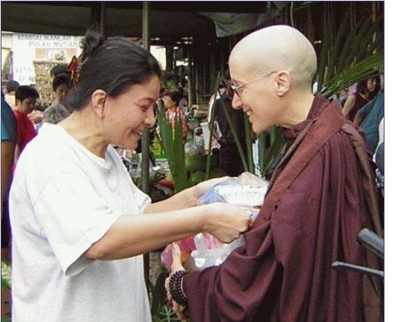 [A smiling woman places a packet of food in Amma's bowl]