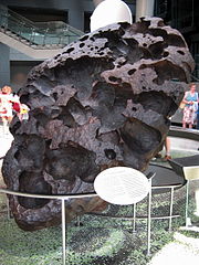  large black egg)shaped boulder of porous structure standing on its top, tilted.